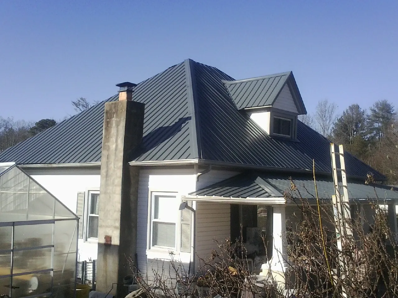 Dark blue standing seam metal roof on a white farmhouse with dormer — Slate & Tile Roof Repair by Roofing Brothers in Union Grove