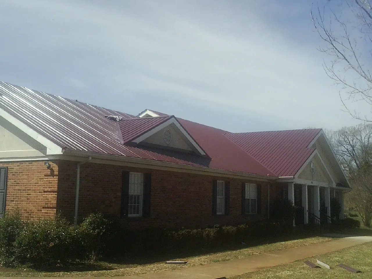 Red metal roof with gabled entries on a long brick building, from a Hail Damage Roof Repair job in Union Grove