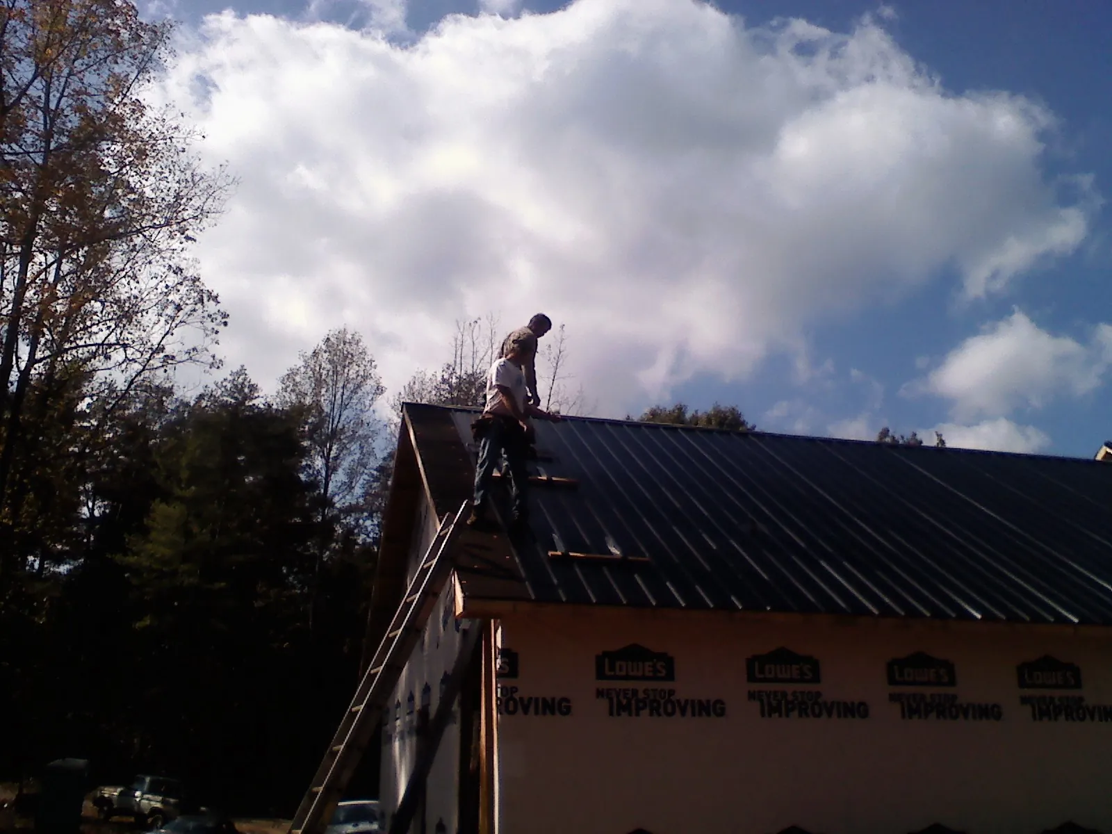 Roofer fastening dark metal panels high against a cloudy sky, from a Roof Inspection job in Union Grove