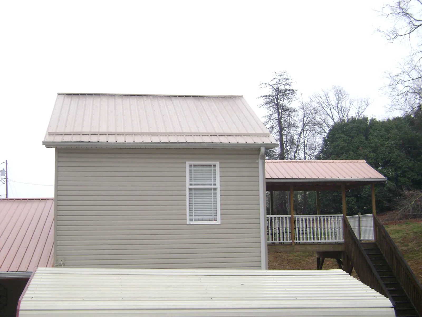 Tan metal roofs on a two story addition and attached porch, from a Roof Replacement job in Union Grove